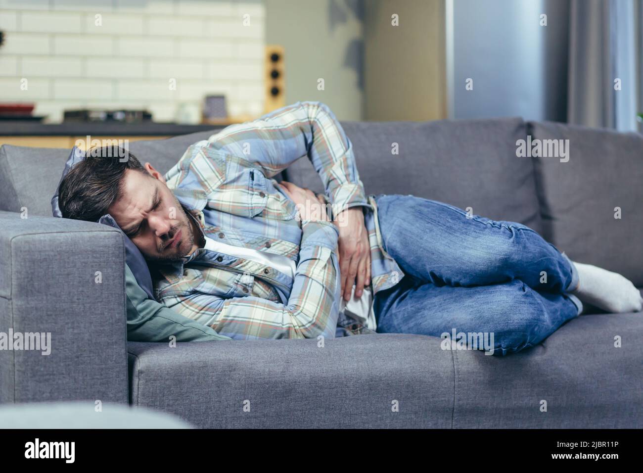 The sick man lying on the couch at home has severe abdominal pain Stock Photo
