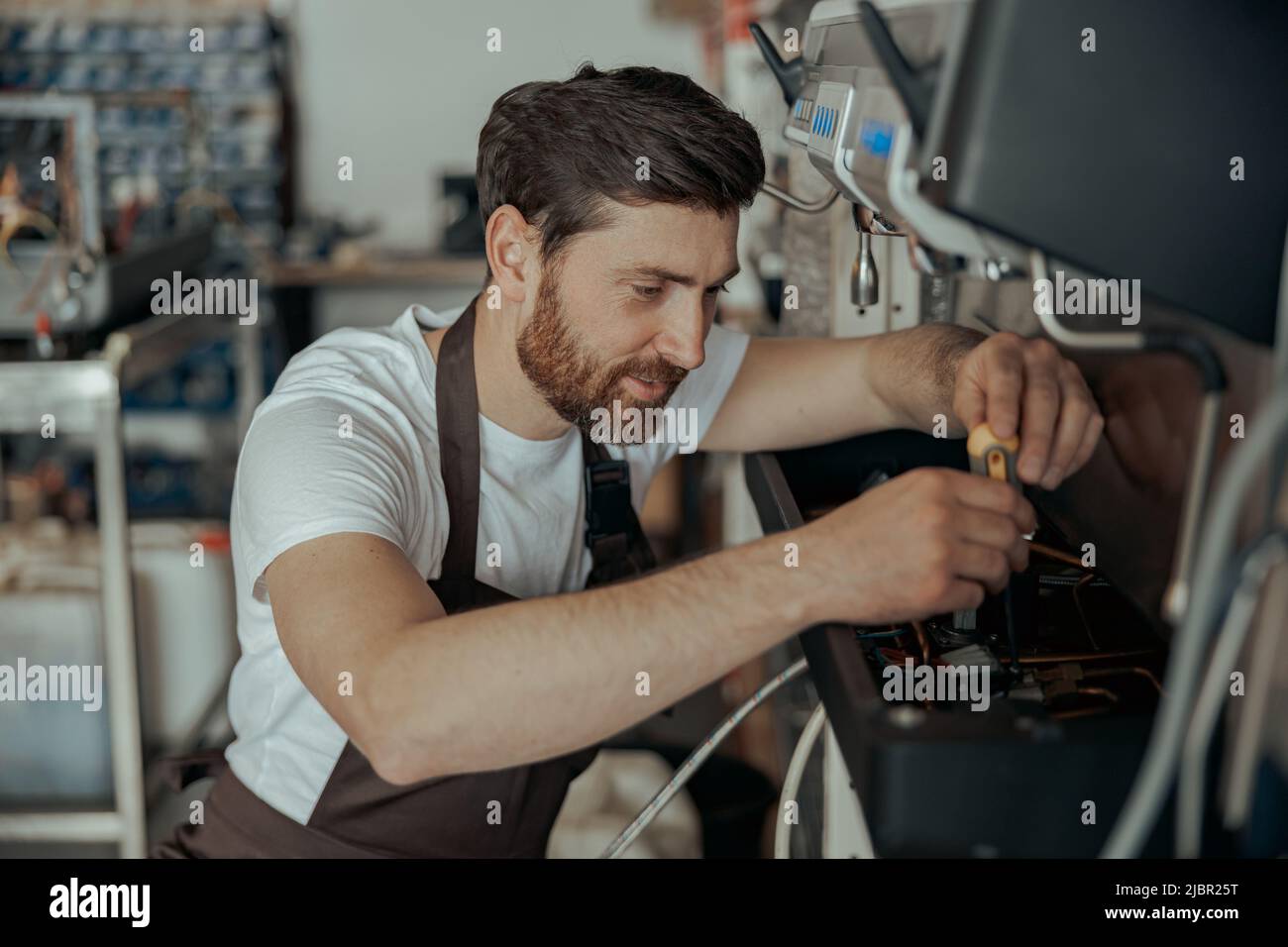Smiling young worker repairing coffee machine in a workshop Stock Photo