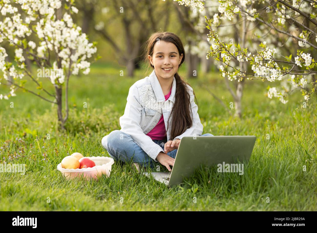 Little girl using laptop computer in a backyard. Child studying at home ...