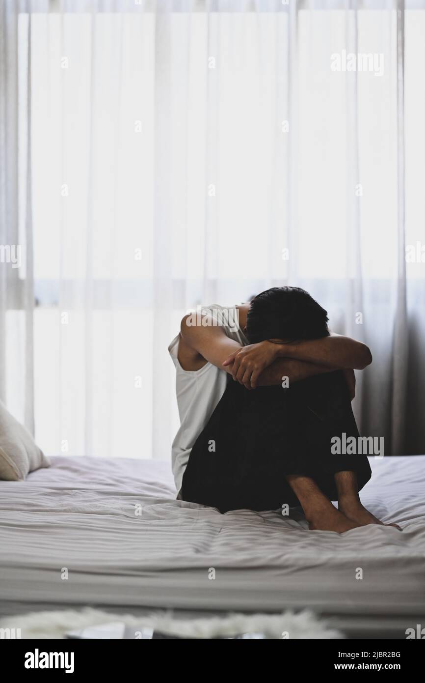 Unhappy man sitting in the dark bedroom with low light environment