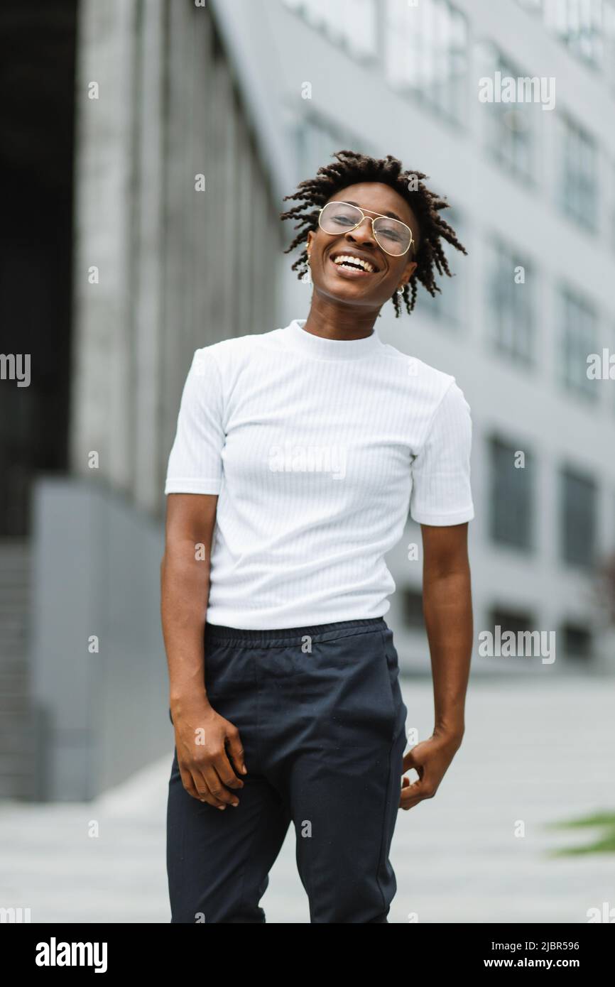Beautiful young african american woman with black curly hairstyle.  Beautiful girl in casual clothes in the street. Happy female wearing white t -shirt and dark pants Stock Photo - Alamy