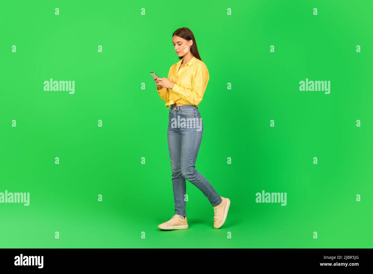 Woman Using Mobile Phone Browsing Internet Walking Over Green Background Stock Photo