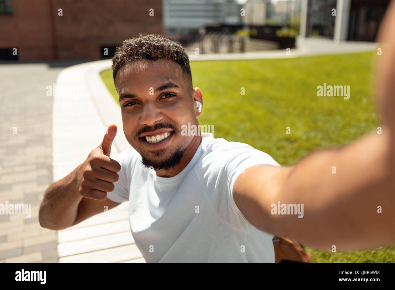 Selfie time. Happy african american man making photo of him and showing thumb up while walking in city park Stock Photo
