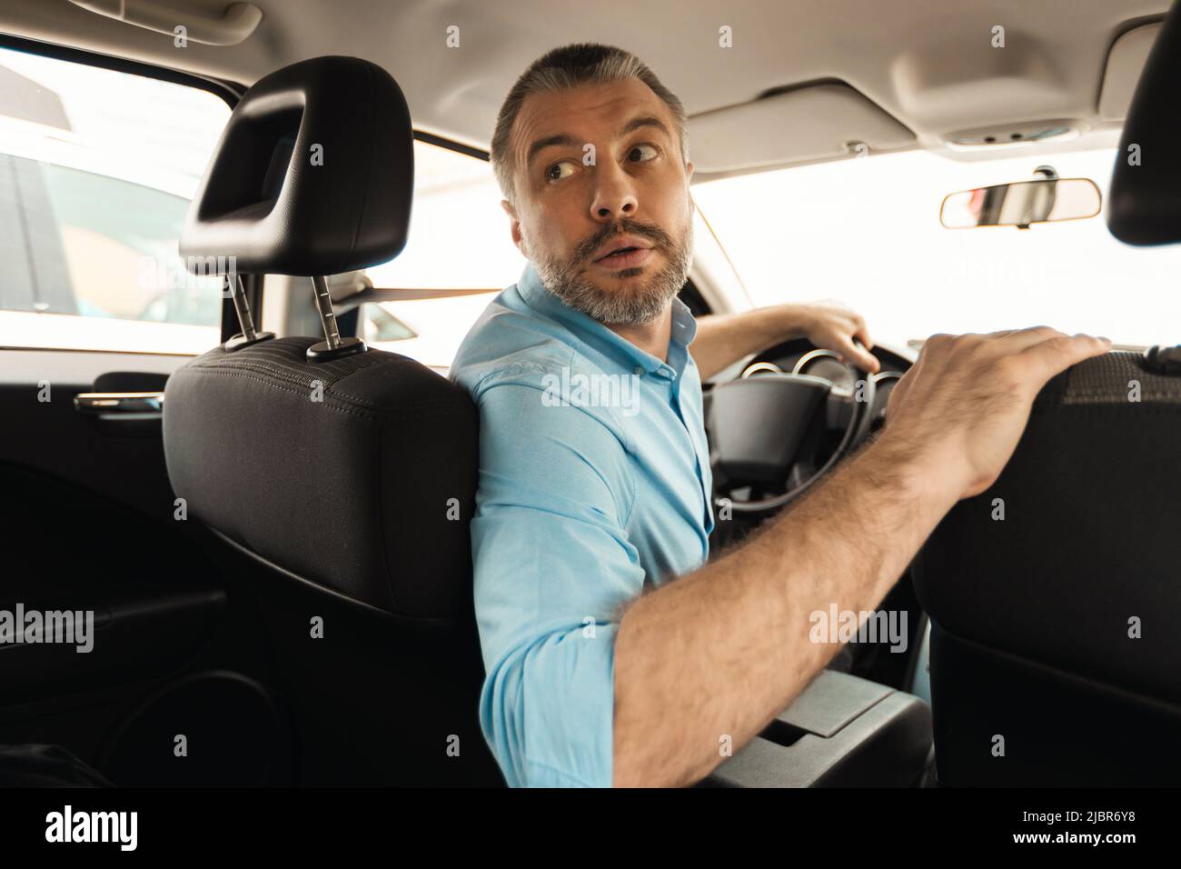 Middle Aged Male Driver Driving Car In Reverse Looking Back Stock Photo