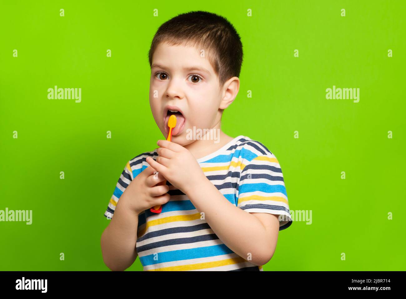 A preschool boy of 4 years cleans with a toothbrush a tongue on a green background. Stock Photo