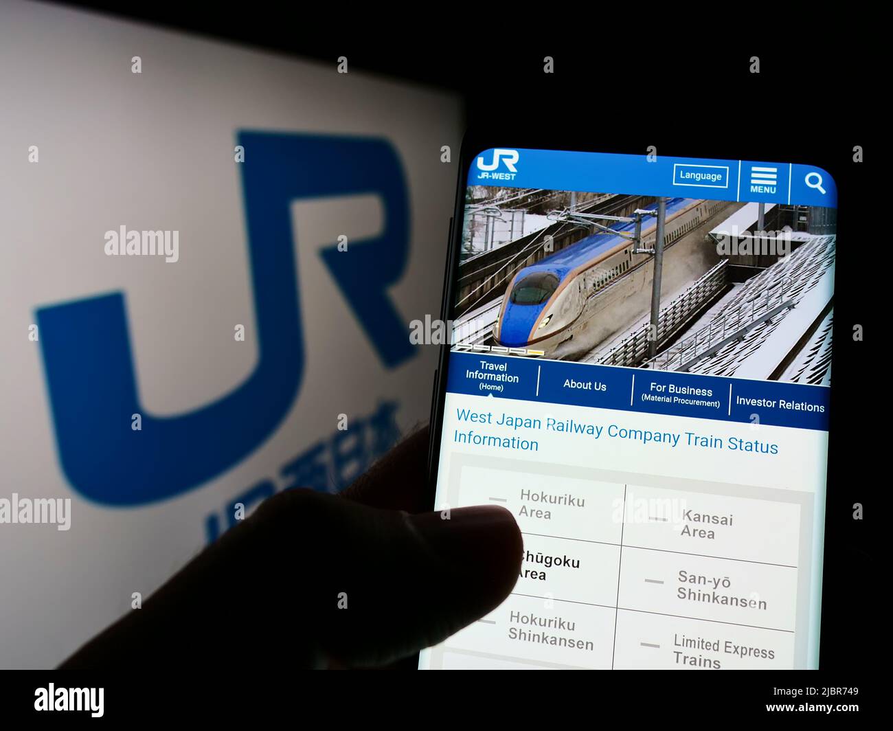 Person holding smartphone with webpage of Japanese company West Japan Railway (JR) on screen in front of logo. Focus on center of phone display. Stock Photo