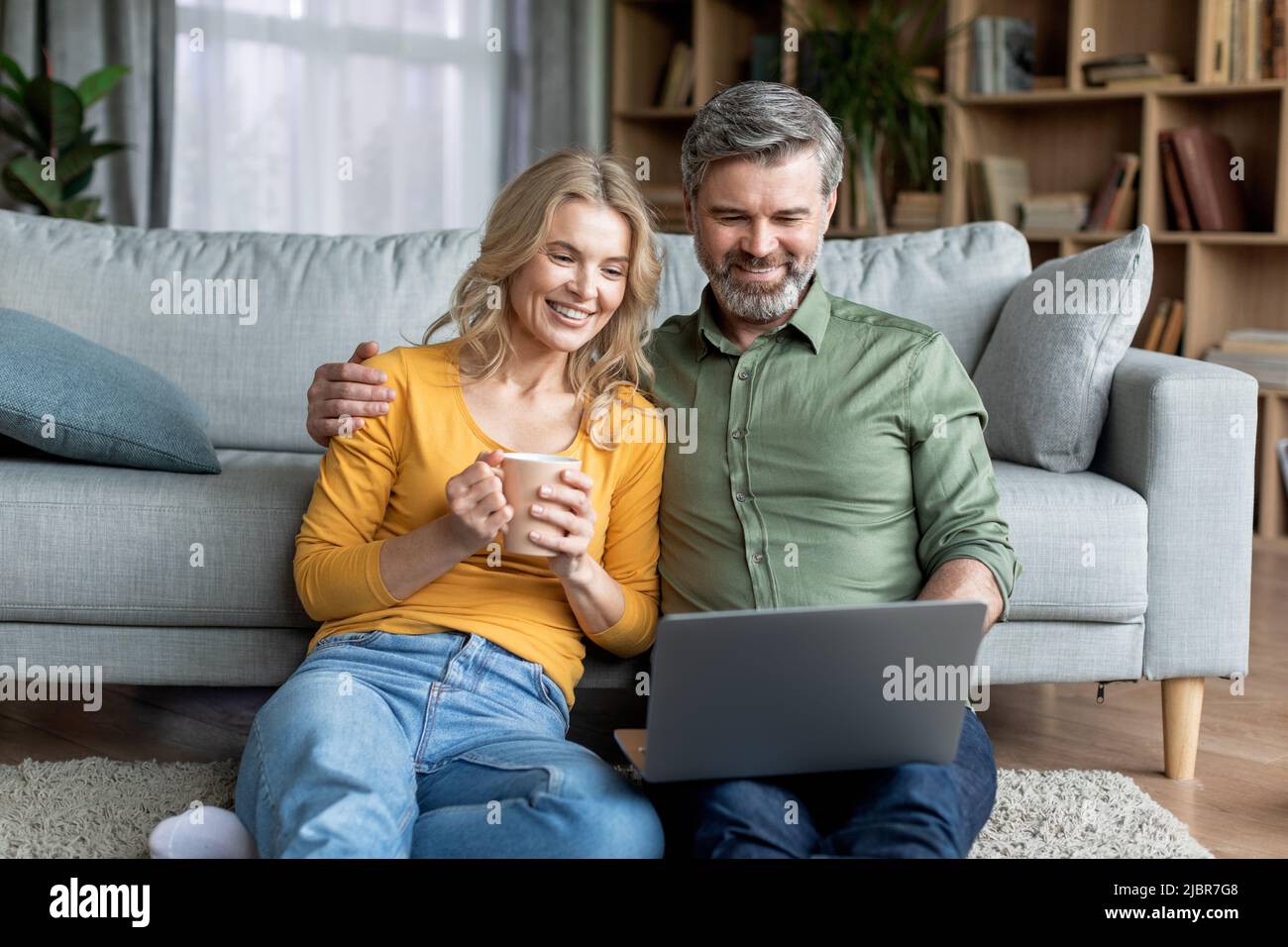 Happy Middle Aged Couple Spending Time With Laptop At Home Stock Photo