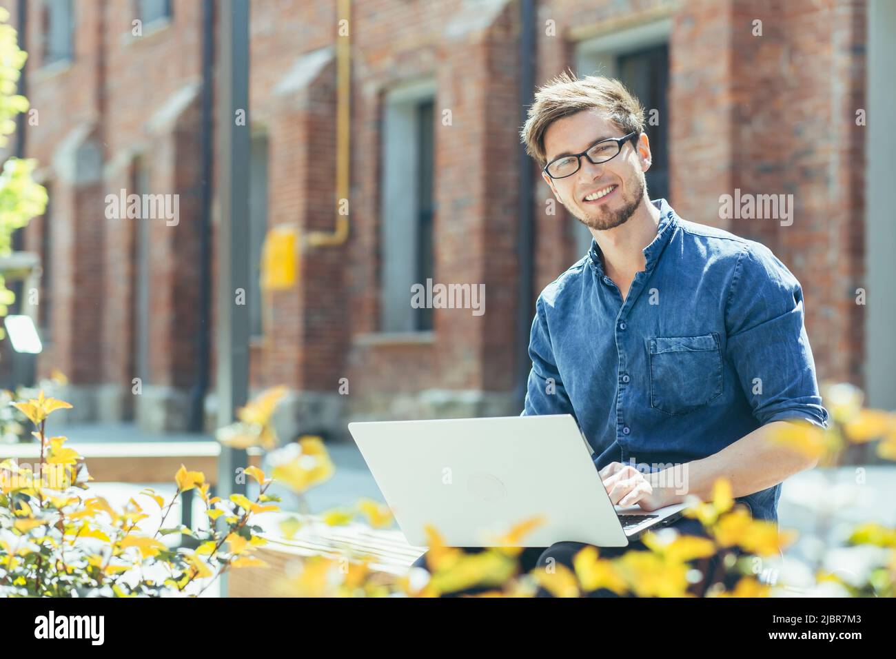 Young businessman with glasses near the office working on a laptop Stock Photo
