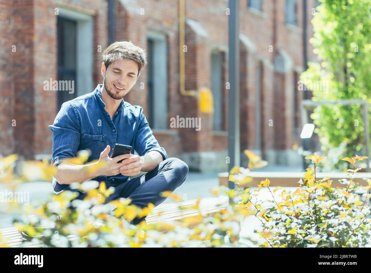 Young man outside student campus, student enjoys phone smiling Stock Photo