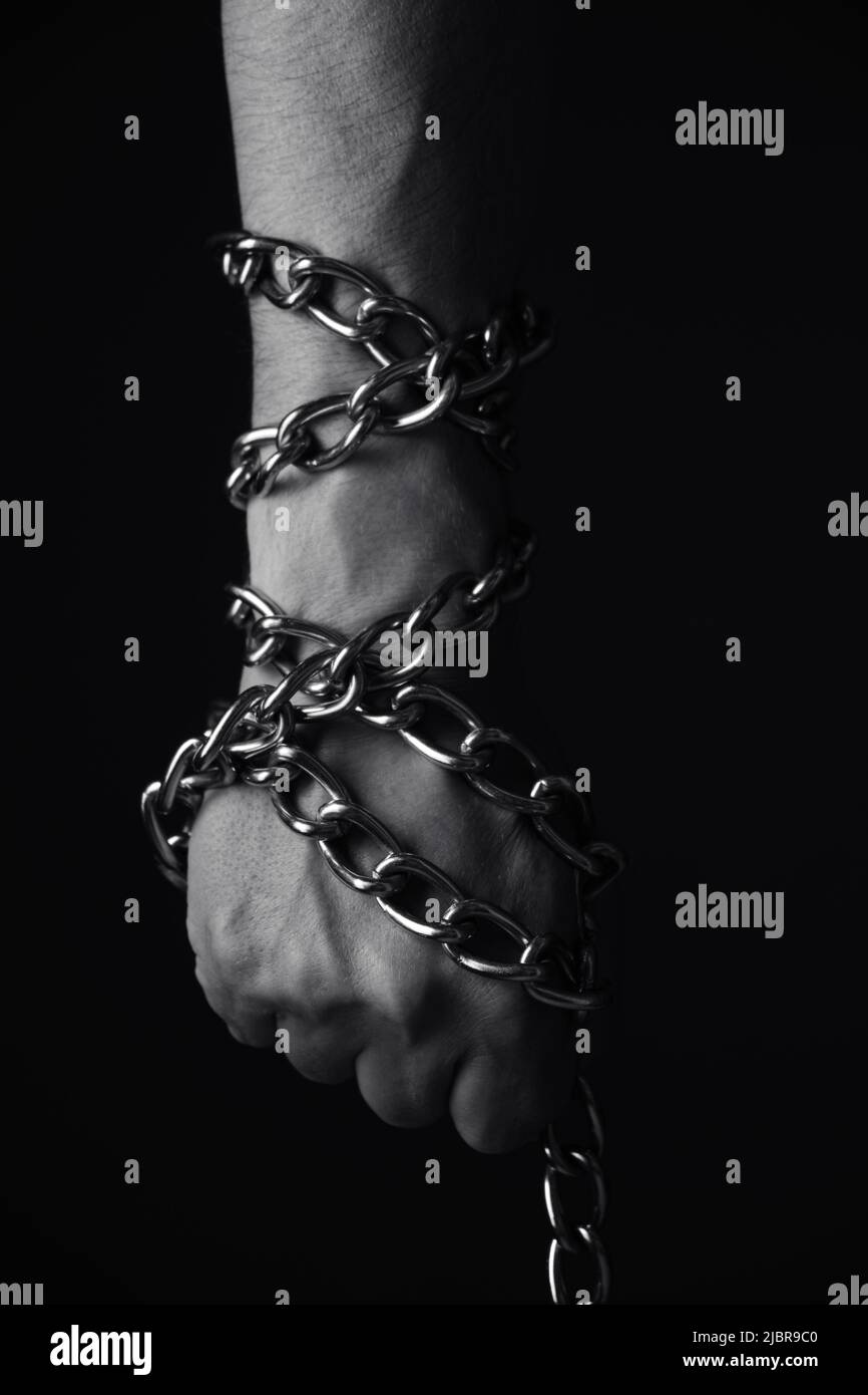 Mans hand entangled with a metal chain, concept slavery, hostage and freedom.Black and white photo. Stock Photo