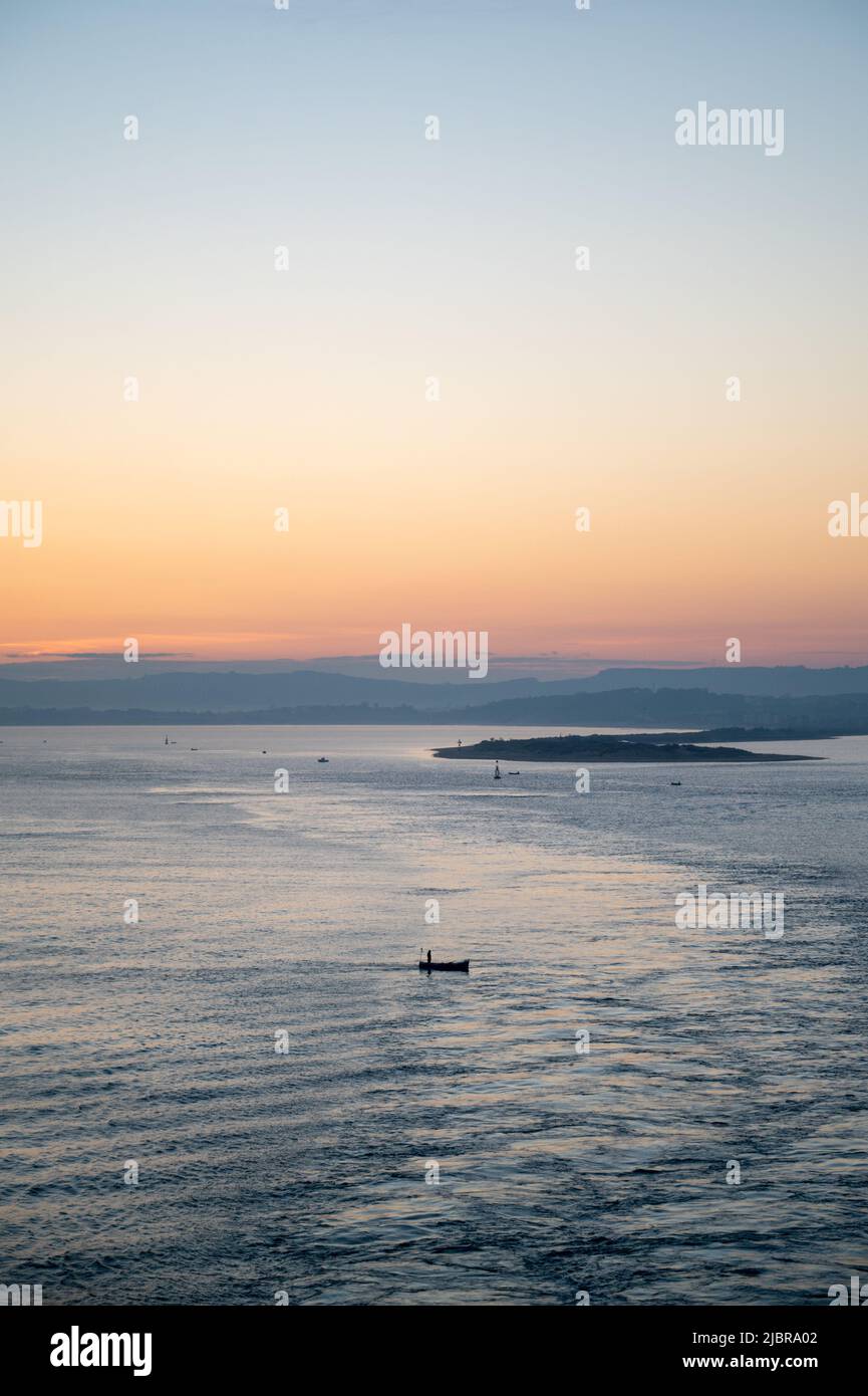 A small fishing boat at dawn in the harbour at Santander Spain dwarfed in the big landscape. Stock Photo