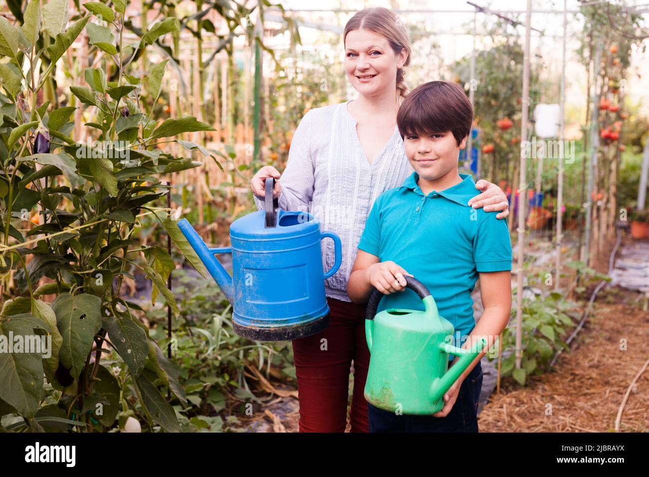 Little boy with mother holding colorful watering pots near seedlings Stock Photo