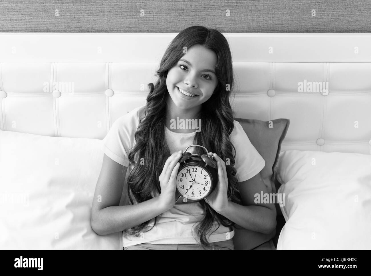 Good morning. Happy kid hold alarm clock in bed. Morning time. Wakening after sleep. Early riser Stock Photo