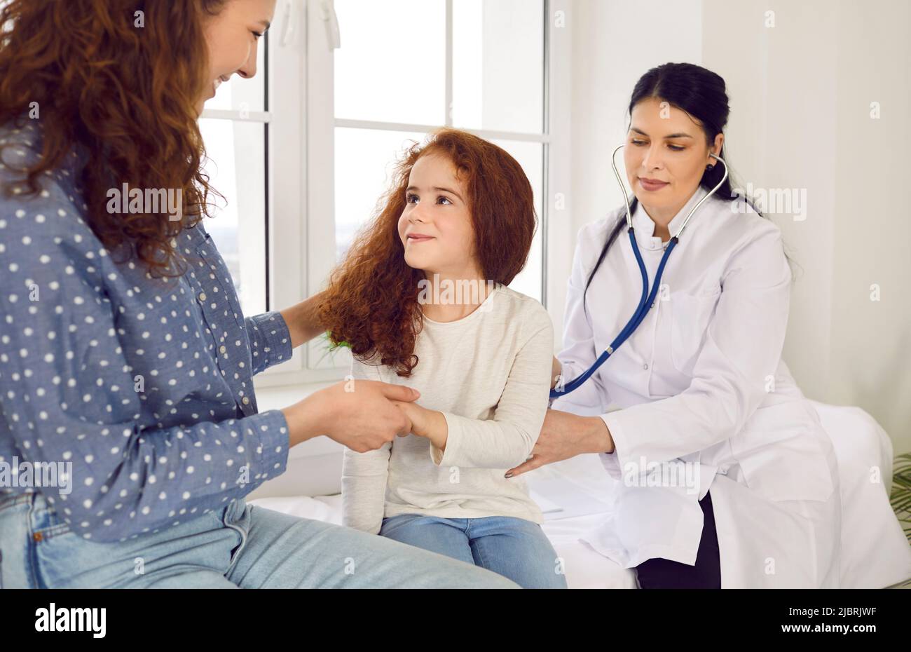 Female doctor puts stethoscope to child's back and listens to breathing and lungs of little girl. Stock Photo