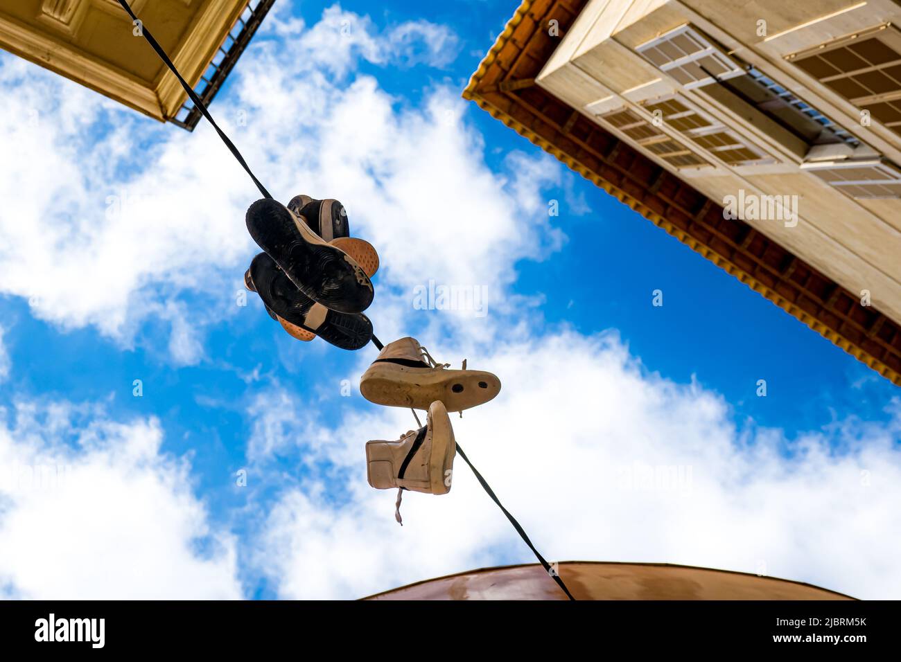 Old sneakers thrown over a telephone wire hanging down in urban environment as a symbol of commemorating a rite of passage or a way to bully someone. Stock Photo