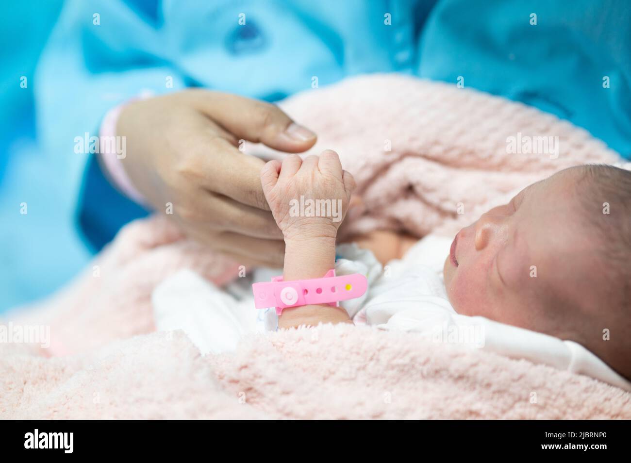mother hand holding their new born baby finger hand closeup ,newborn Sleeping in her hug in hospital Stock Photo