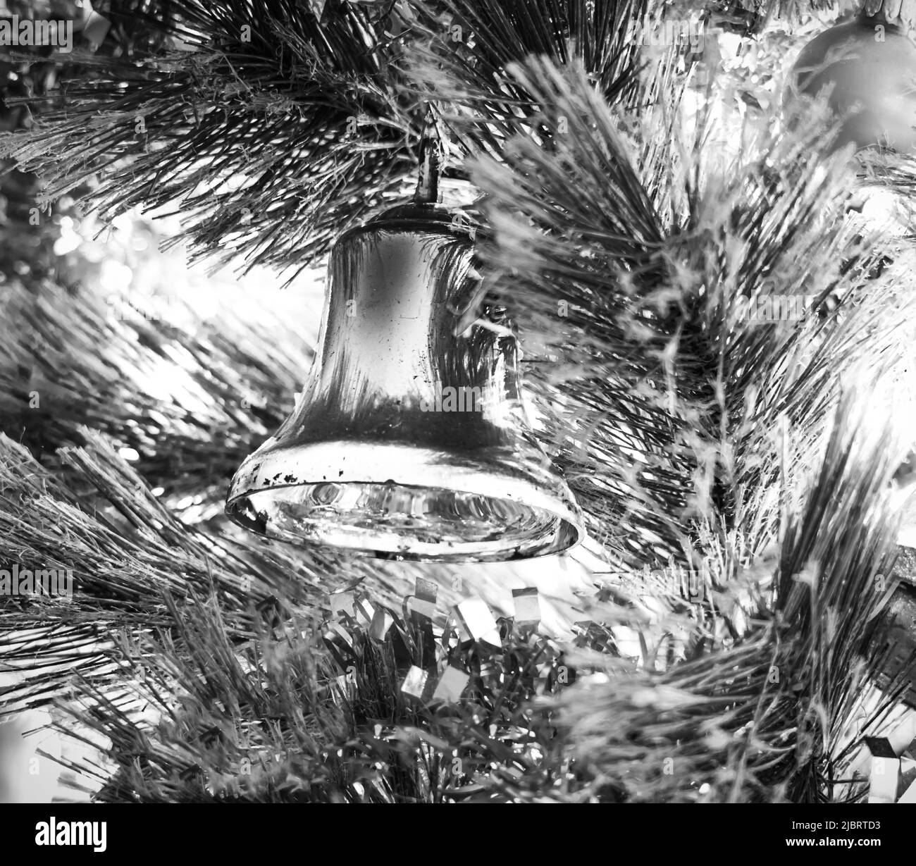Shiny metallic silver bell Christmas ornament hanging in a lighted Christmas tree in black and white Stock Photo