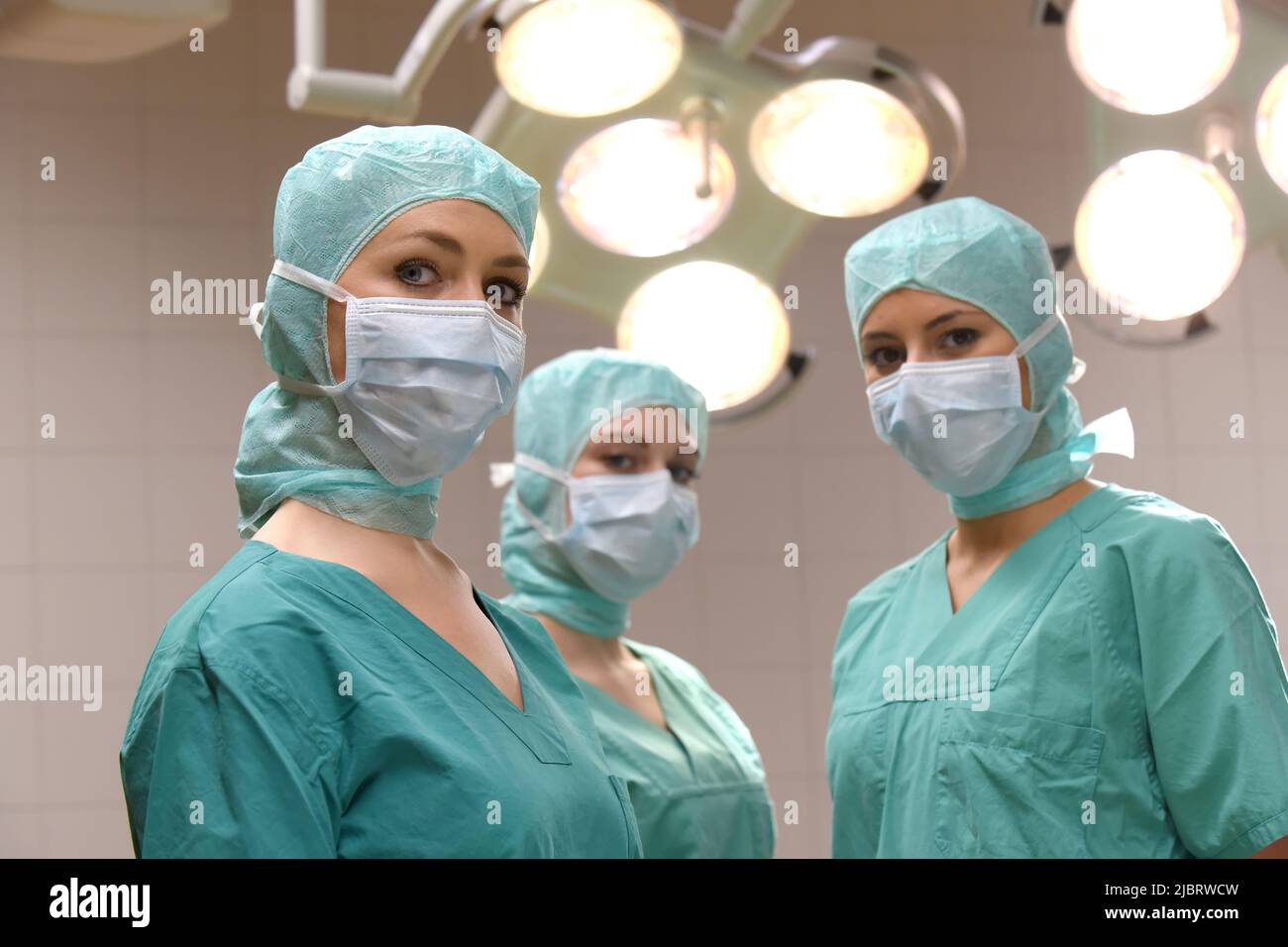 Three nurses are seen in a surgical operation theater.  They are dressed as a operation theater nurses with  face masks  and sterile surgical clothing Stock Photo