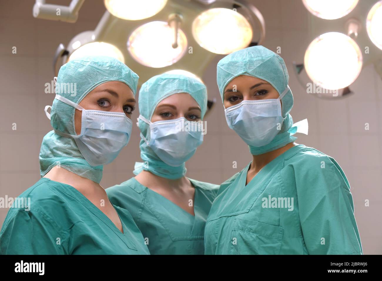 Three nurses are seen in a surgical operation theater.  They are dressed as a operation theater nurses with  face masks  and sterile surgical clothing Stock Photo