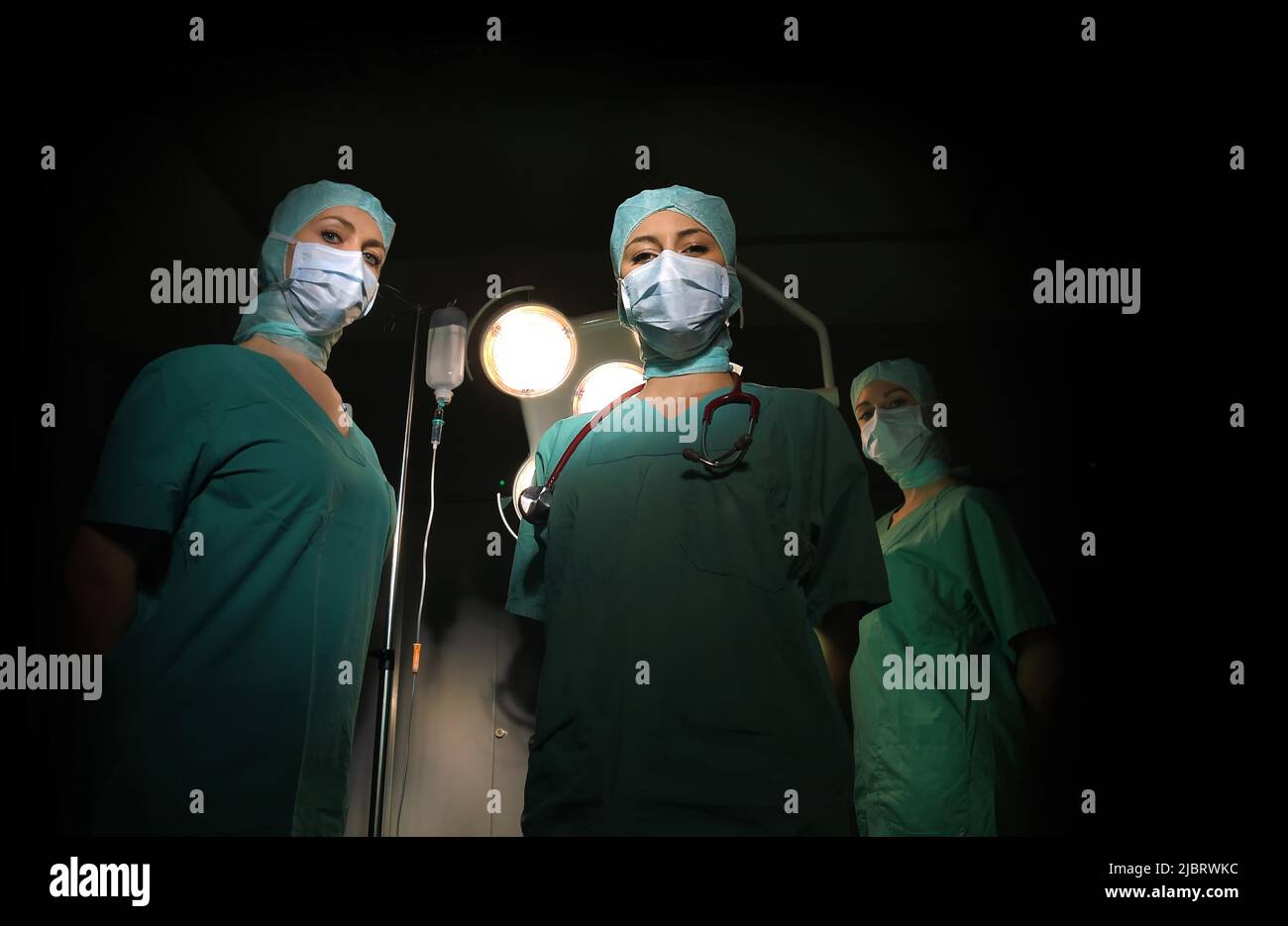 Three nurses are seen in a surgical operation theater.  They are dressed as a operation theater nurses with  face masks  and sterile surgical clothing Stock Photo