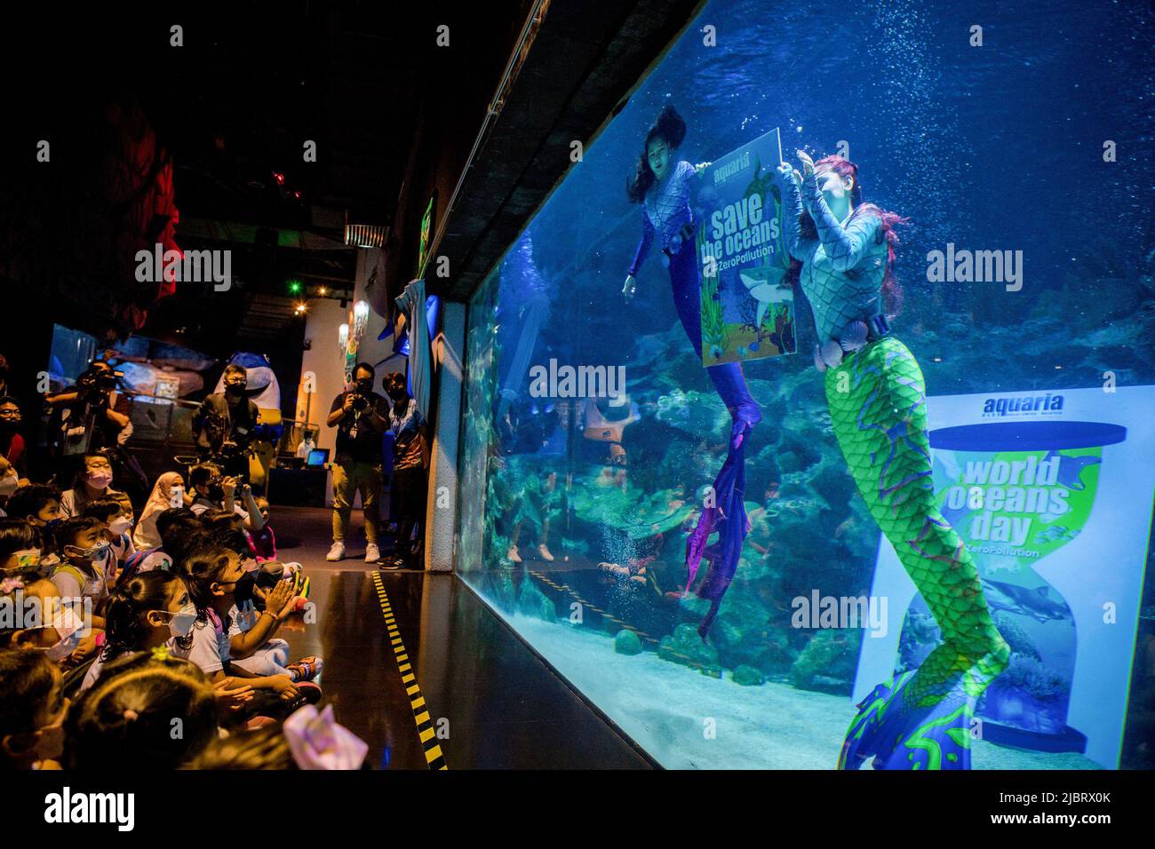 Kuala Lumpur, Malaysia. 08th June, 2022. Two performers wearing mermaid costumes are seen swimming in the main aquarium of Aquaria KLCC while holding the 'save the ocean' banner for a special performance on the occasion of the World Ocean Day in Kuala Lumpur. Credit: SOPA Images Limited/Alamy Live News Stock Photo