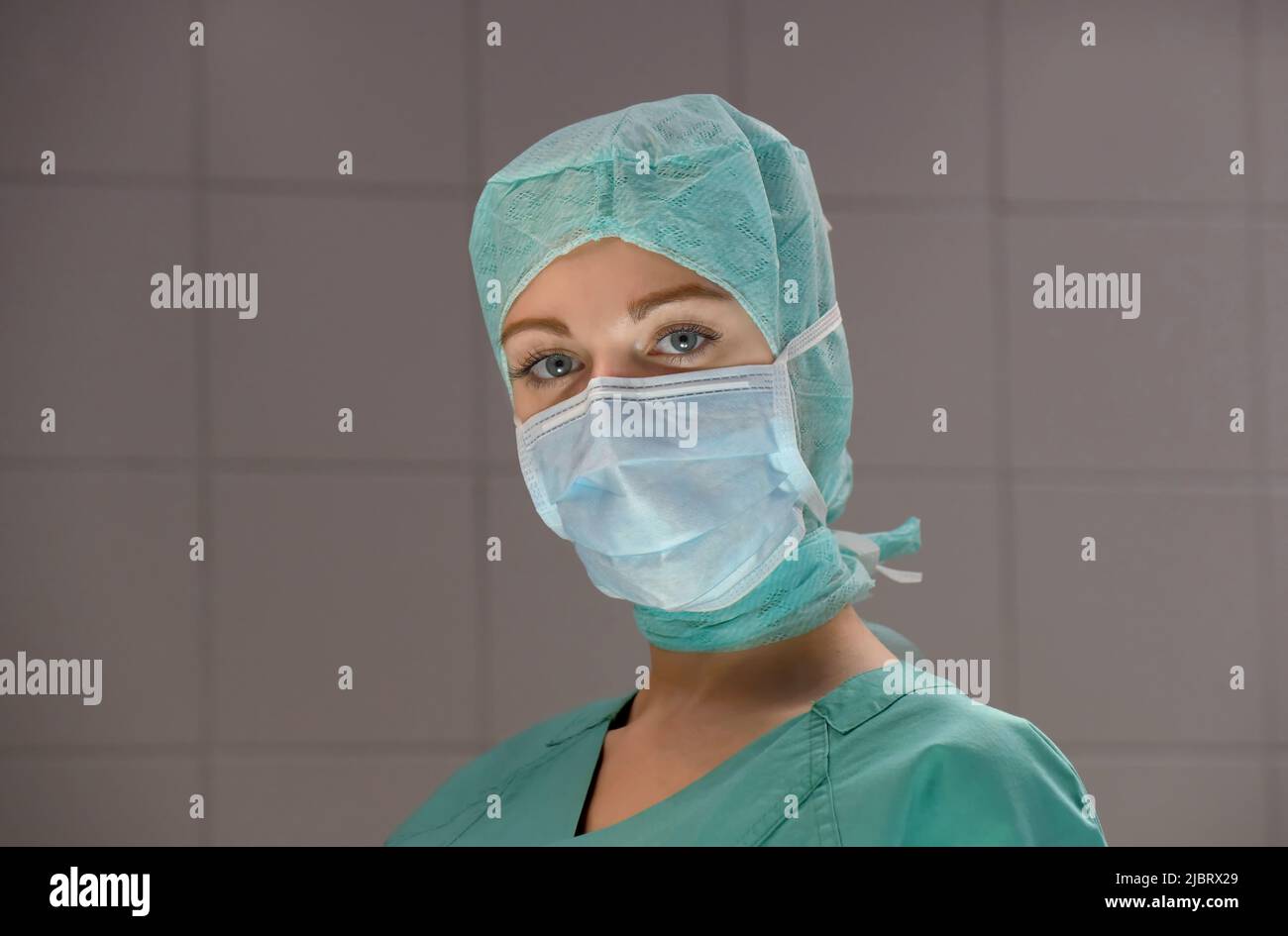 A young woman is seen in an hospital operation theater.  Fully dressed as a theater nurse with a face mask  and green sterile medical work clothing. Stock Photo