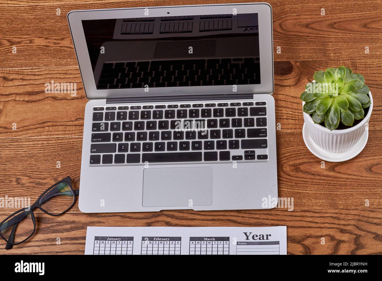 Top view open macbook air laptop pc with glasses and plant. Brown