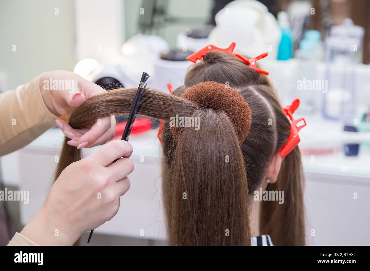 Close-up of the master's hands combing a lock of hair on a woman's head. The hairdresser makes a hairstyle for a young woman. Barber shop, business concept. Beauty salon, hair care. Stock Photo
