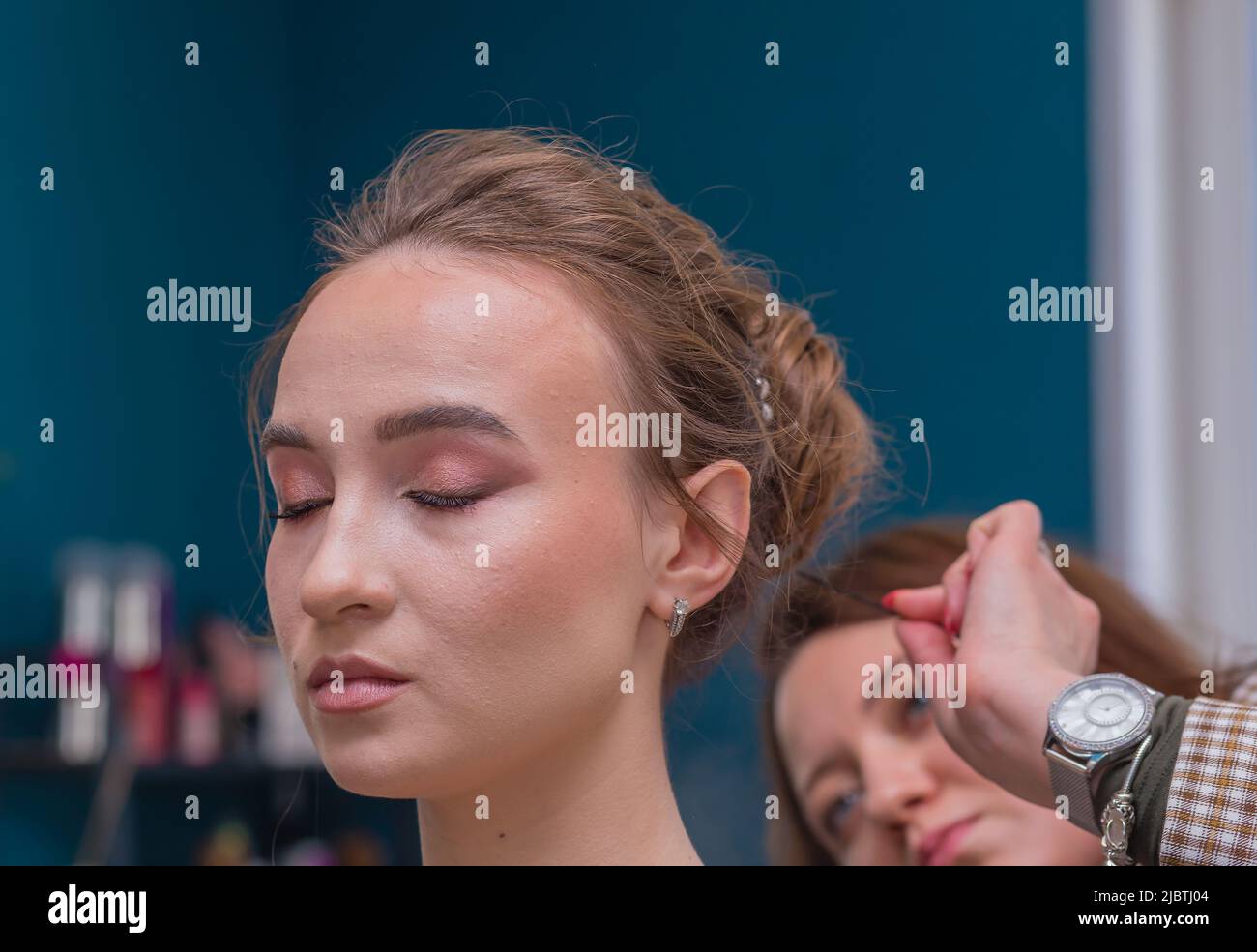 The face of a client's girl, from behind the master examines her hair in defocus. The hairdresser makes a hairstyle for a young woman. Barber shop, business concept. Beauty salon, hair care. Stock Photo