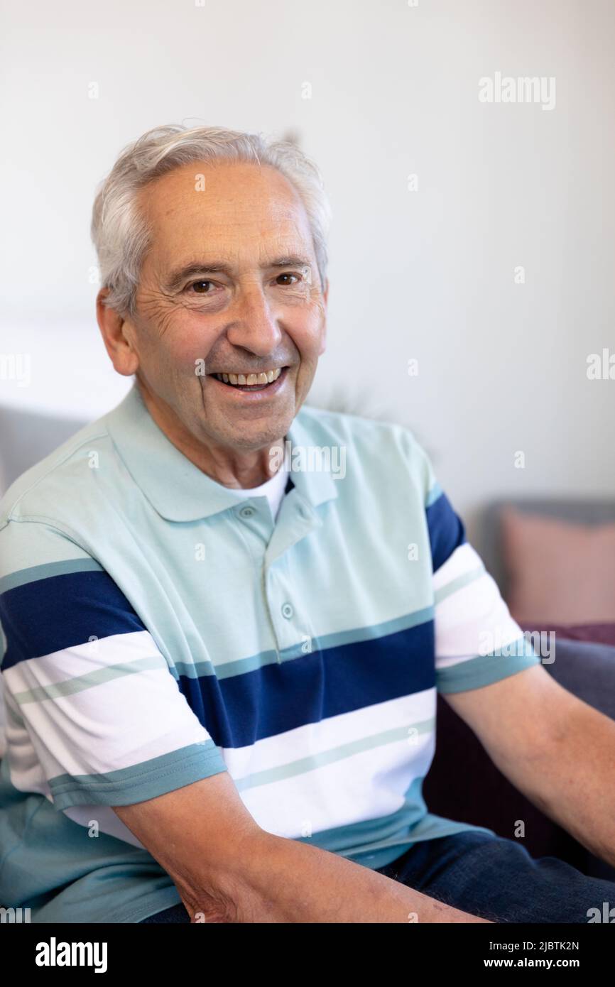 Portrait of smiling caucasian senior man sitting on sofa against white wall in living room Stock Photo