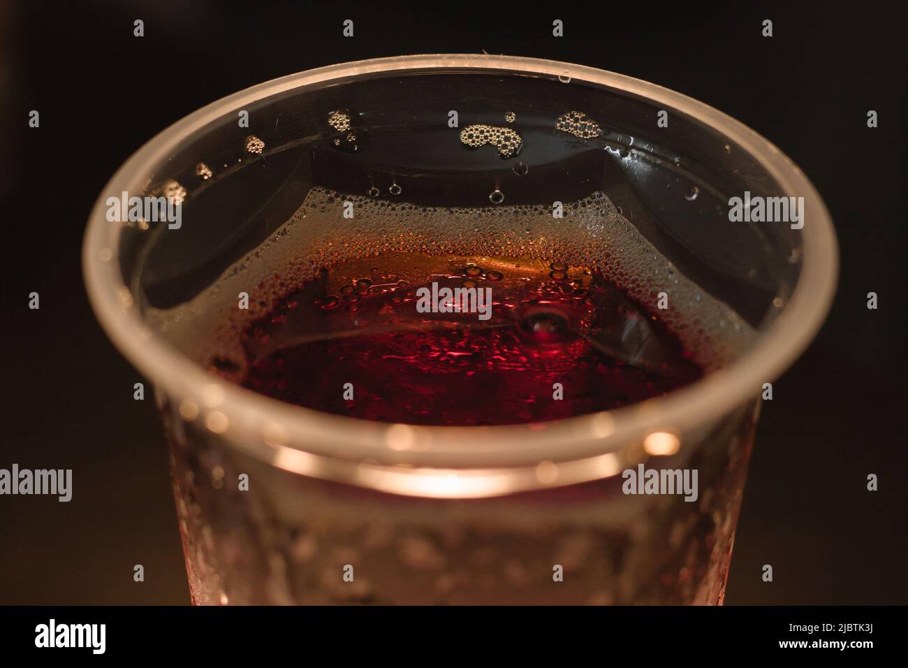 Cola with fizz in a plastic glass. Closeup, night. Stock Photo