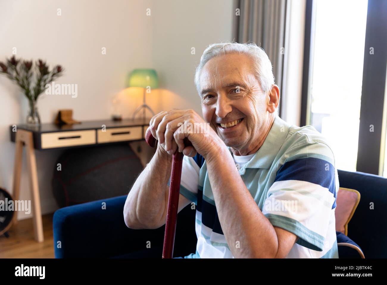 Portrait of smiling caucasian senior man with walking cane sitting on chair in living room at home Stock Photo