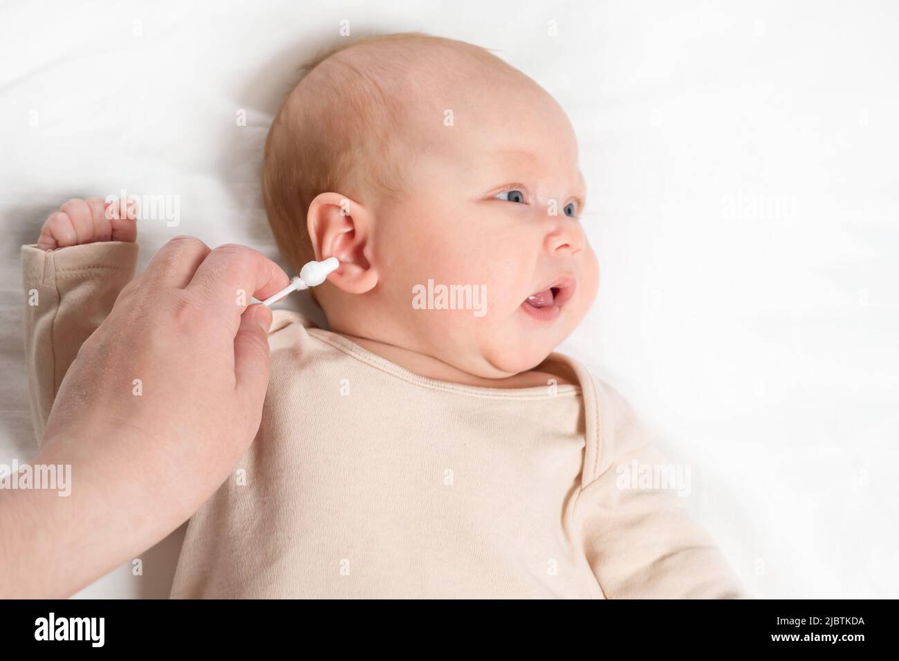 Hand of mother cleans ears of baby girl with cotton swab Stock Photo
