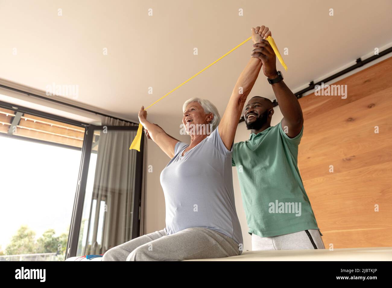African american male physiotherapist helping senior woman to exercise with resistance bands Stock Photo
