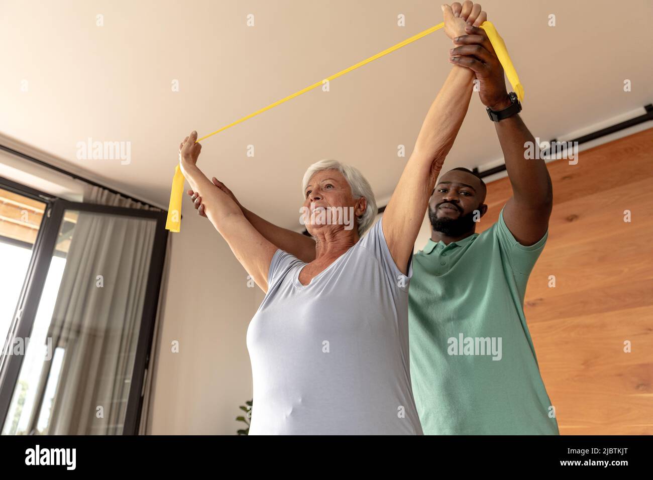 African american male physiotherapist helping senior woman to exercise with resistance bands Stock Photo