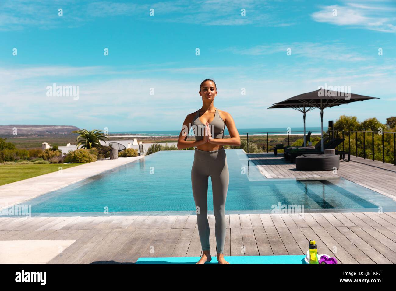 Caucasian young woman practicing yoga and meditating near the pool Stock Photo