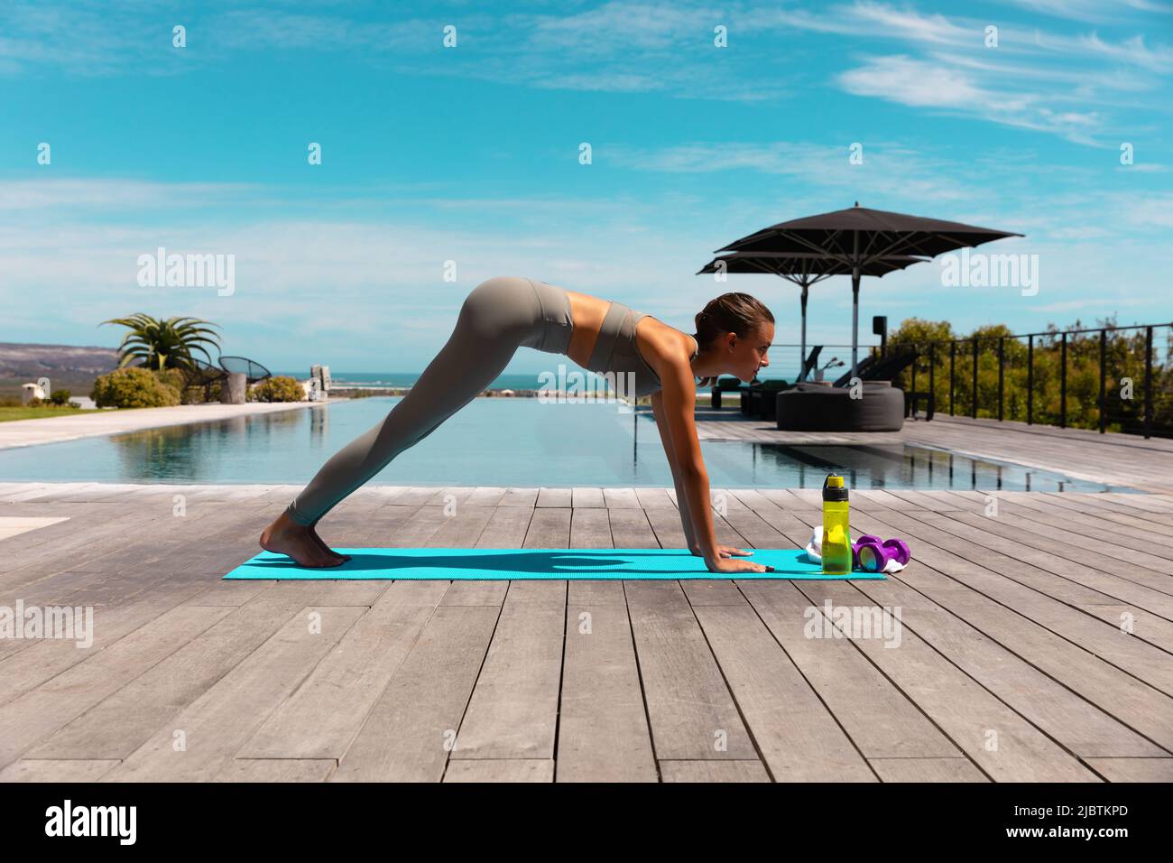 Caucasian young woman practicing yoga and meditating near the pool Stock Photo