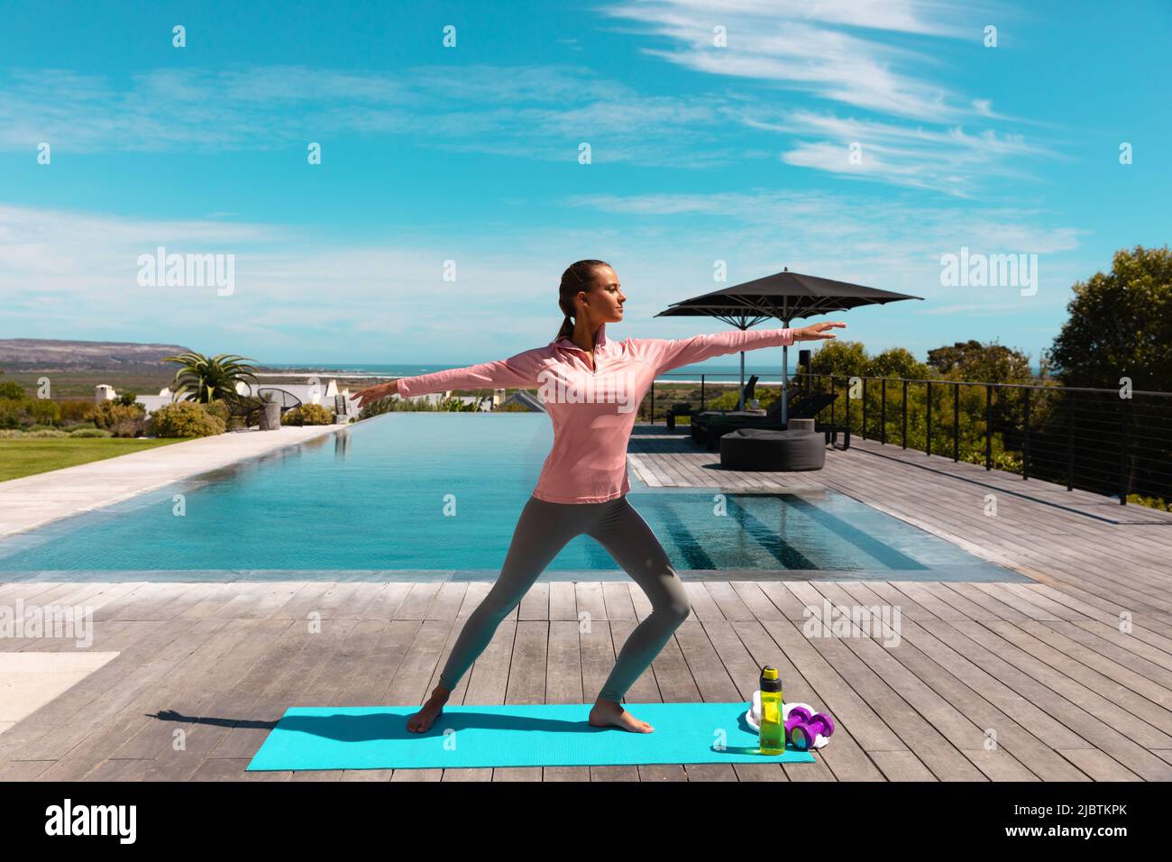 Caucasian young woman practicing yoga and meditating near the pool Stock Photo