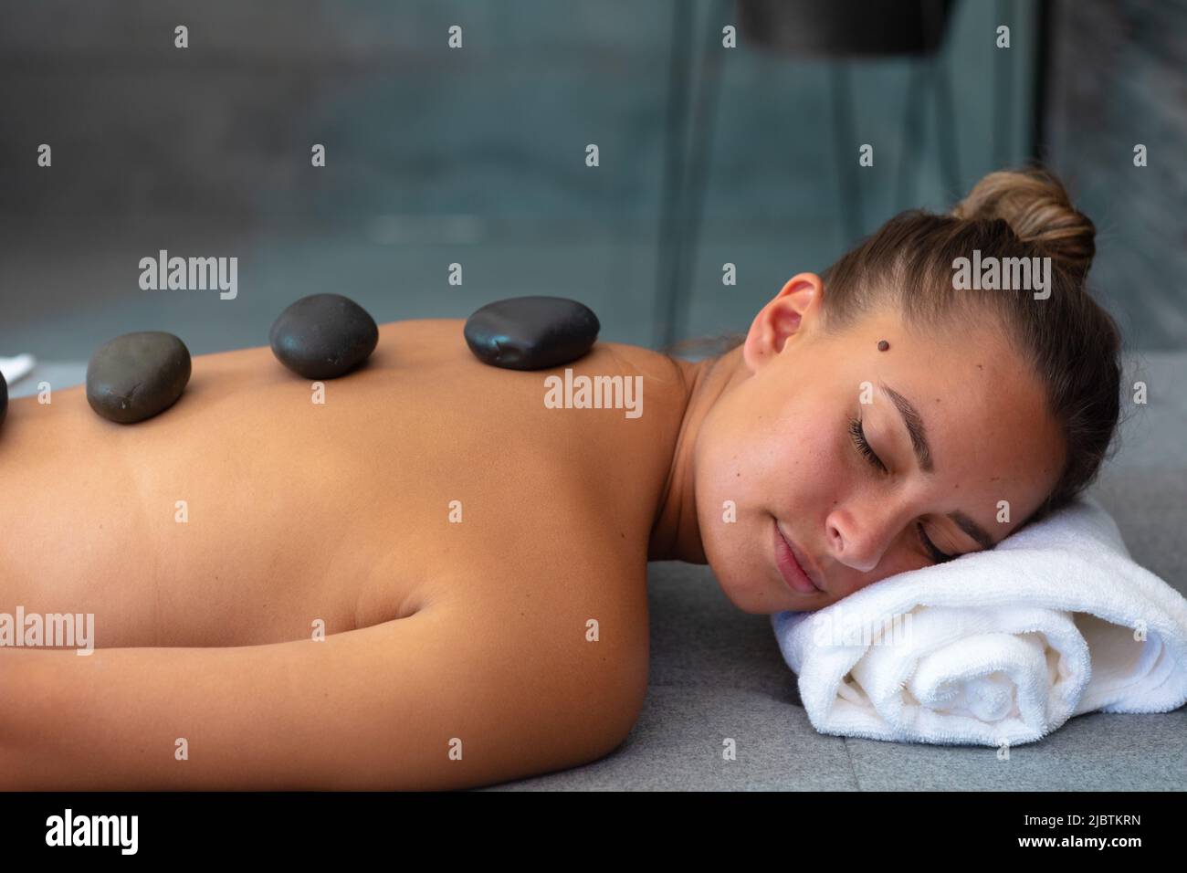 Caucasian young woman with eyes closed receiving hot stone massage at home Stock Photo