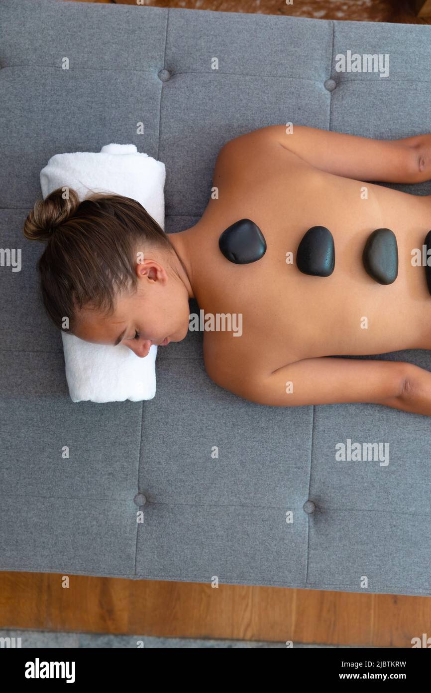 Caucasian young woman with eyes closed receiving hot stone massage at home Stock Photo
