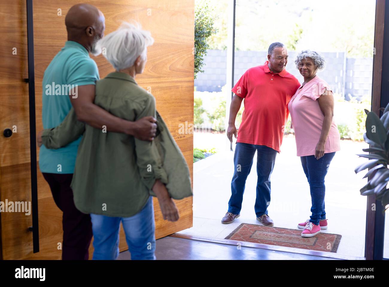 Multiracial seniors welcoming friends while standing at open entrance in retirement home Stock Photo