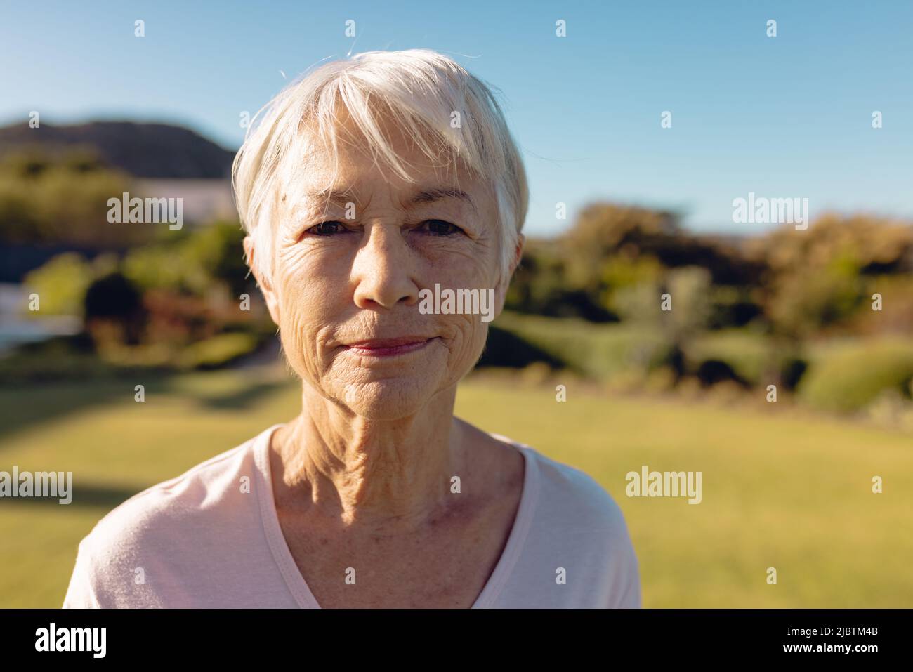 Close-up portrait of asian senior woman with short hair against clear blue sky in yard on sunny day Stock Photo