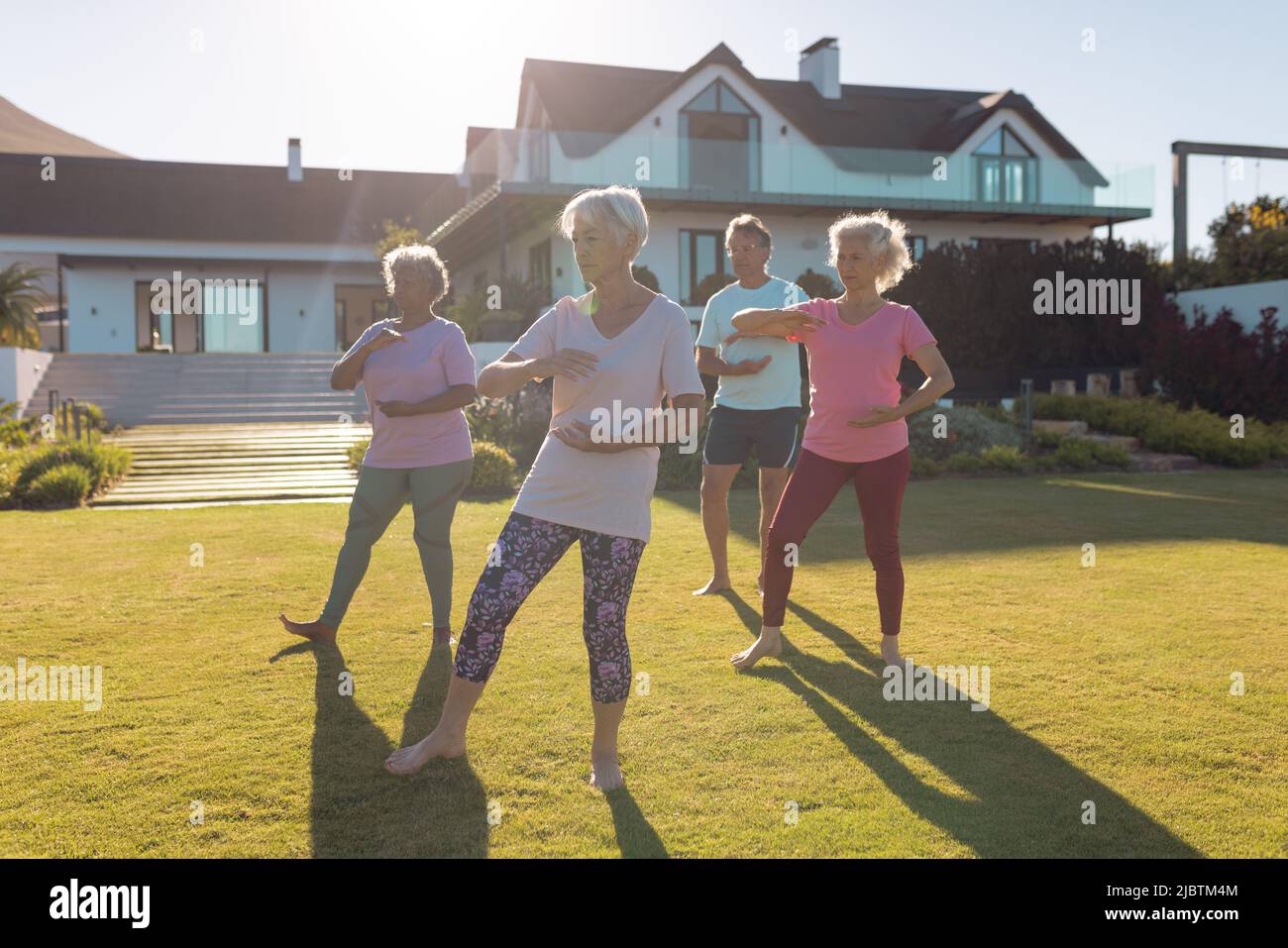 Multiracial male and female seniors exercising on grassy land in yard against retirement home Stock Photo