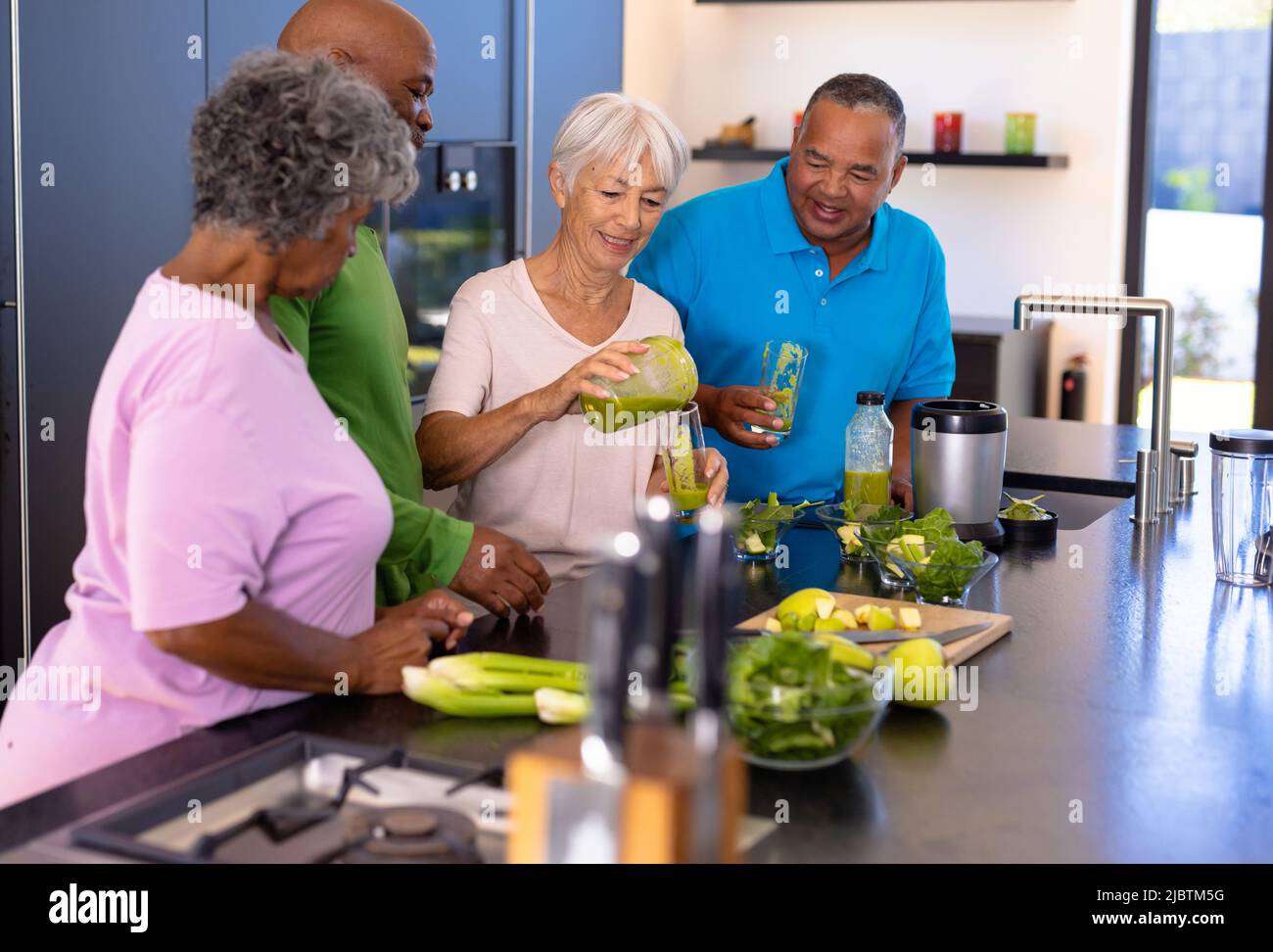 Asian senior woman pouring smoothie in glasses for multiracial friends in kitchen at retirement home Stock Photo