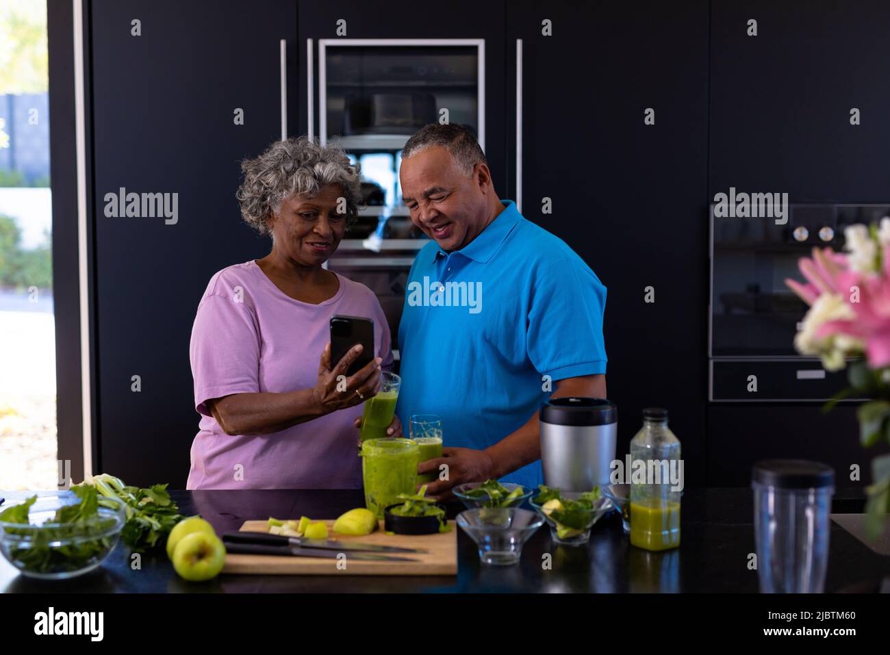 African american senior woman showing mobile phone to caucasian man in kitchen at retirement home Stock Photo