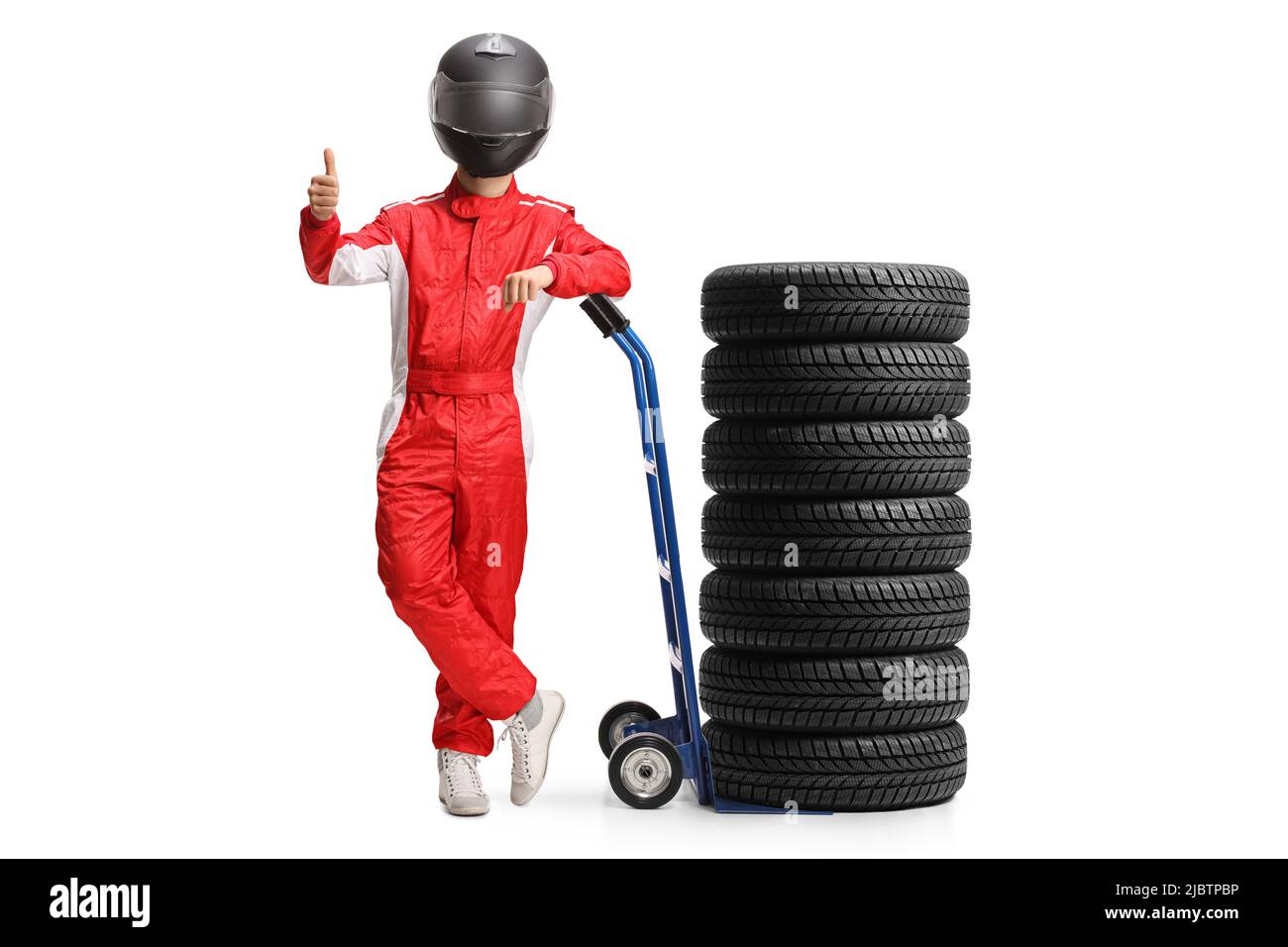 Full length portrait of a racer with a helmet leaning on a hand truck with tires and gesturing thumbs up isolated on white background Stock Photo