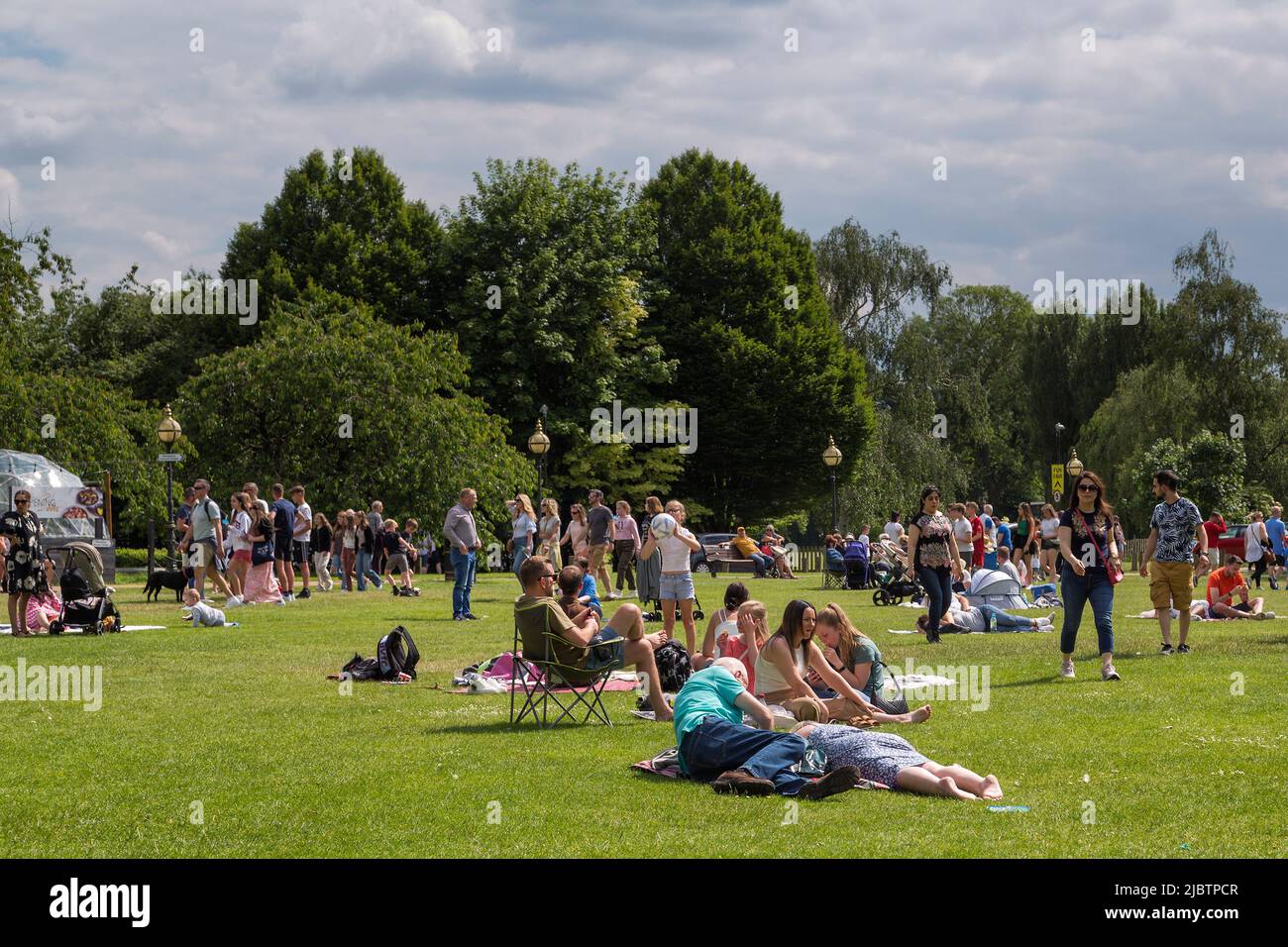 Adults and children socialise, play games and enjoy the weather in a park on a sunny day, Stock Photo