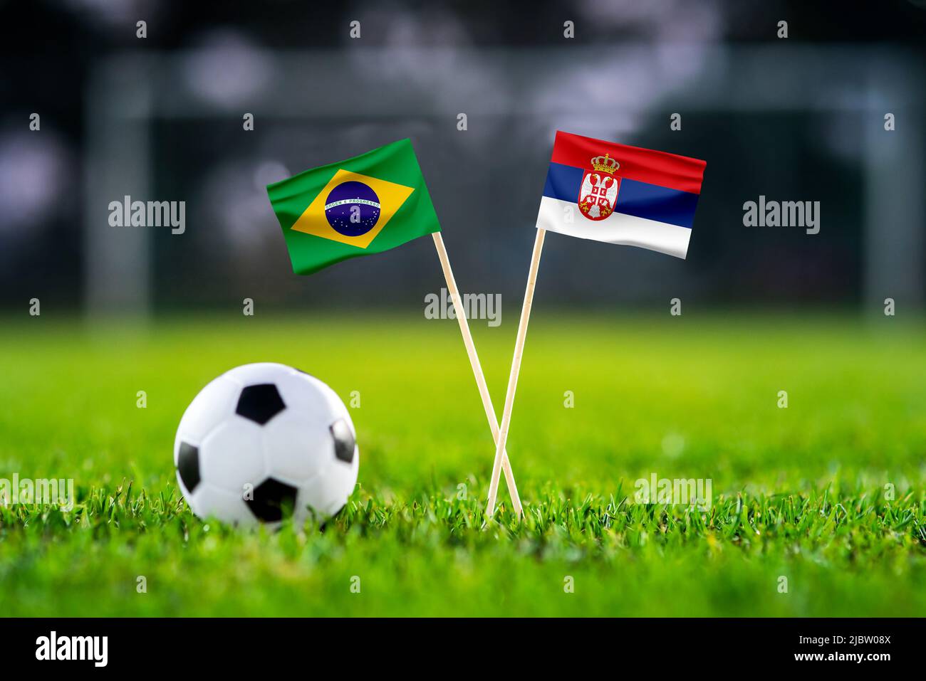 Brazil vs. Serbia, Lusail, Football match wallpaper, Handmade national flags and soccer ball on green grass. Football stadium in background. Black edi Stock Photo