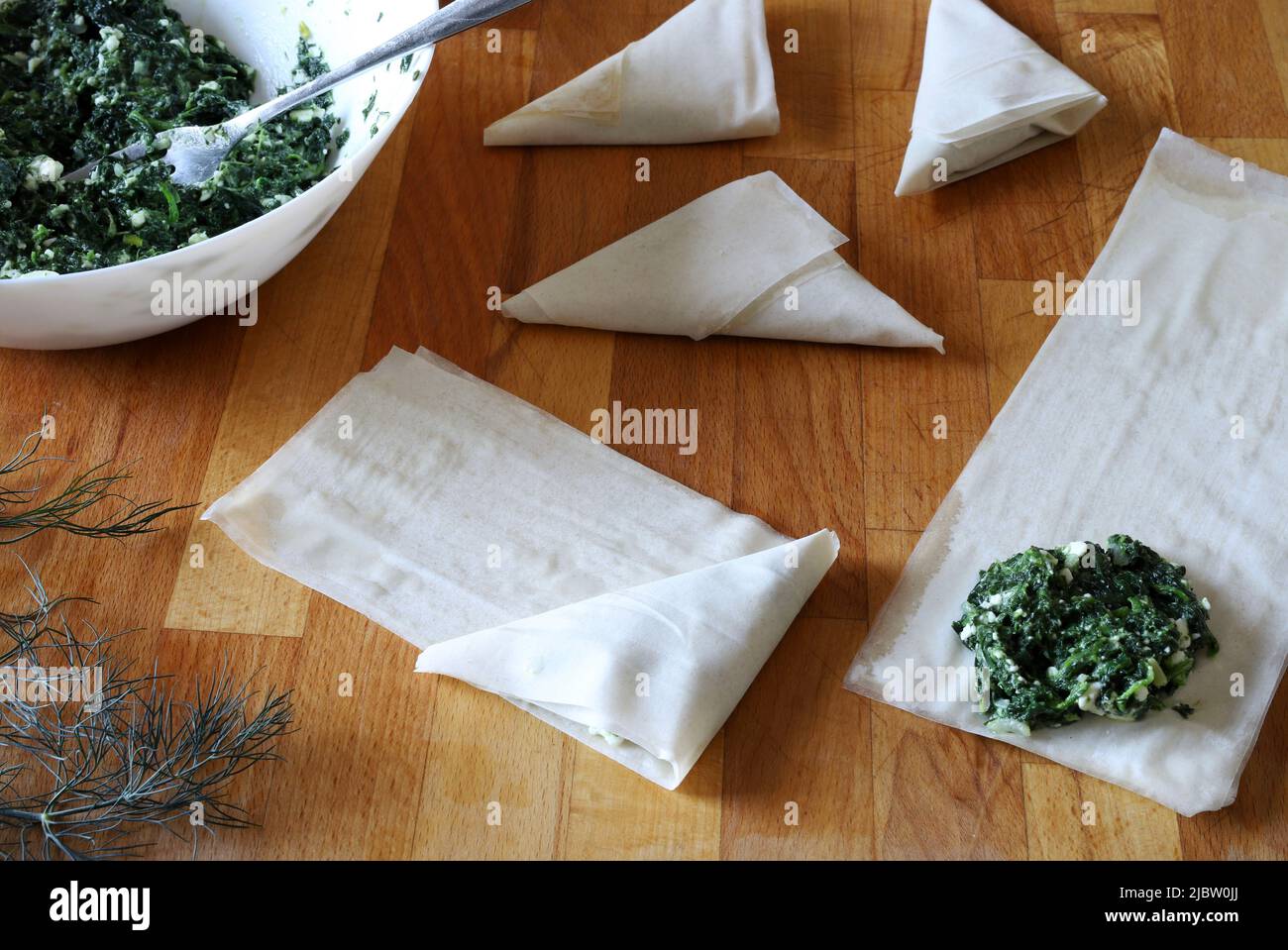 Preparing traditional Greek spinach pie triangles named Spanakopita. Directly above Stock Photo