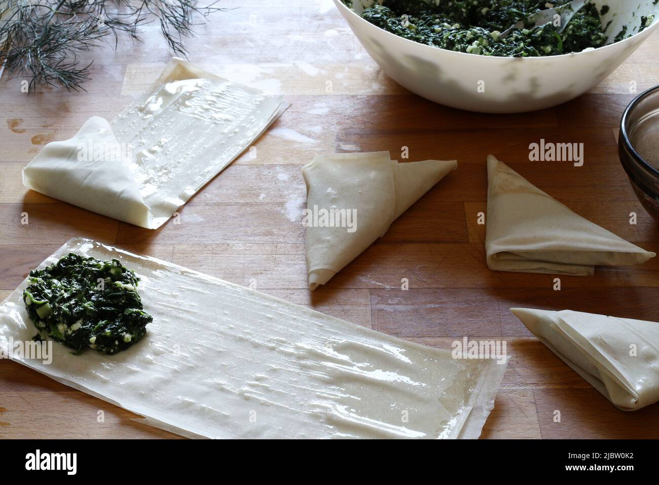 Preparing traditional Greek spinach pie triangles named Spanakopita. Directly above Stock Photo